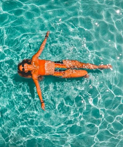 A person lounging in a turquoise ocean, floating on their back with arms and legs spread, sunlit water patterning around them.
